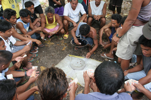 Gambling makes waiting for the cockfighting shorter. Bet for the right side of these three coins and win all. Malapascua. Philippines.